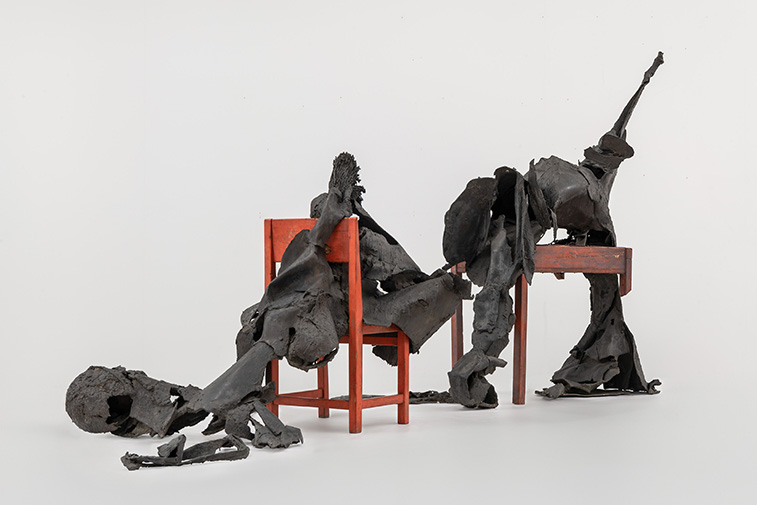 Beeld van Wessel Couzijn, zwarte hangende figuren over een rode stoel en tafel
