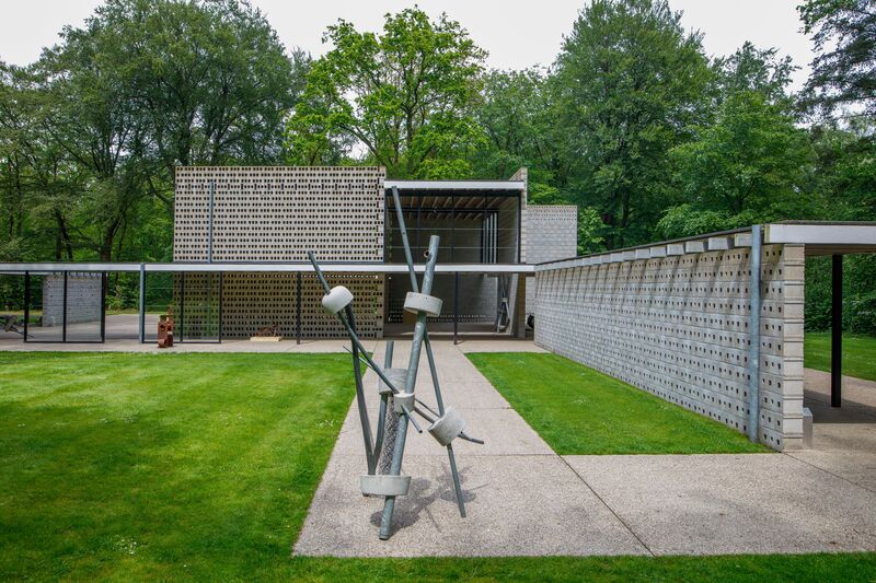 Foto van een modern paviljoen in de beeldentuin van Gerrit Rietveld, met op de voorgrond een kunstwerk gemaakt van ijzeren buizen en ronde vormen van Ruud Kuijer