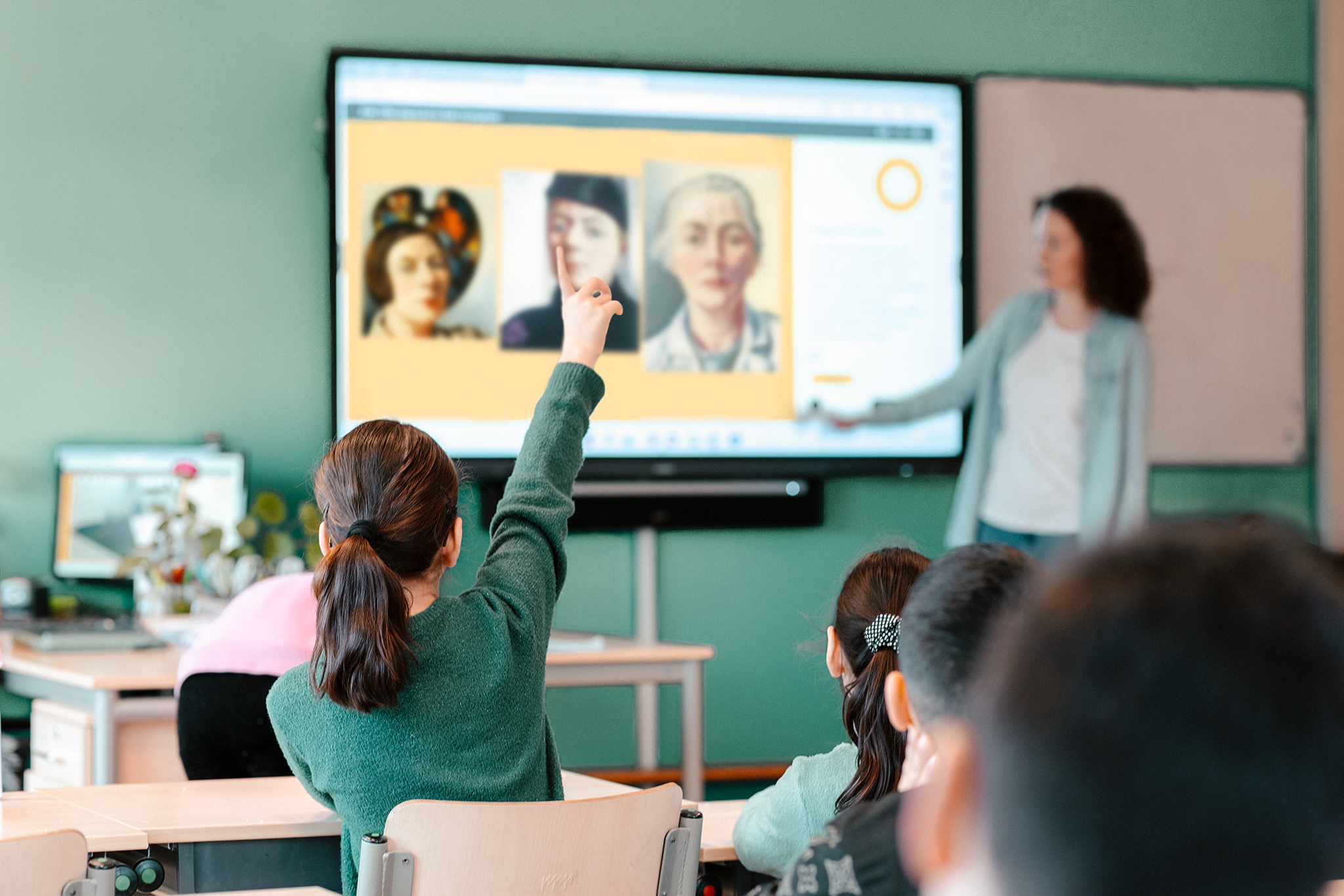 leerkracht bij smartboard, op de voorgrond kind met hand omhoog gestoken