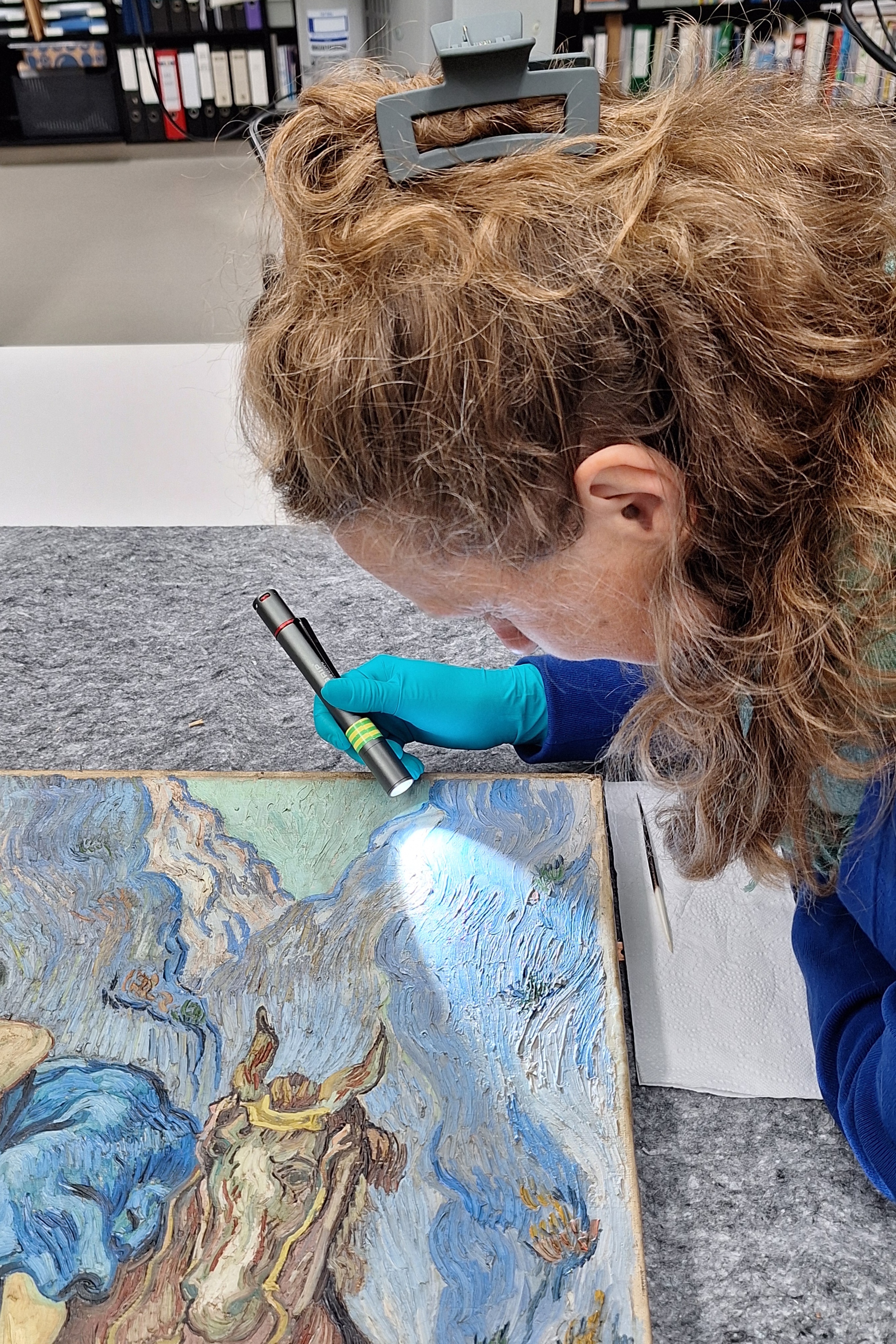 restaurator onderzoekt met een kleine lamp een schilderij van Van Gogh